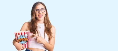 Güzel beyaz kadın elinde patlamış mısırla gülümsüyor. 