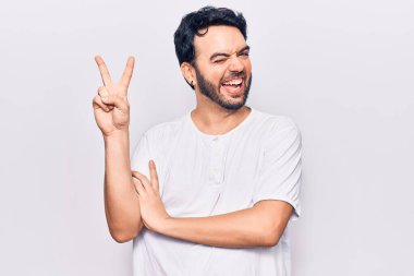 Gündelik kıyafetler giyen, gülümseyen ve kameraya göz kırpan genç İspanyol adam zafer işareti yapıyor. İki numara.. 