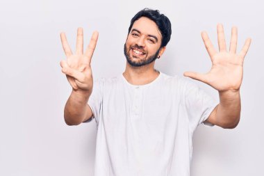 Gündelik kıyafetler giyen genç İspanyol adam sekiz numarayı gösterip işaret ederken kendinden emin ve mutlu bir şekilde gülümsüyor.. 