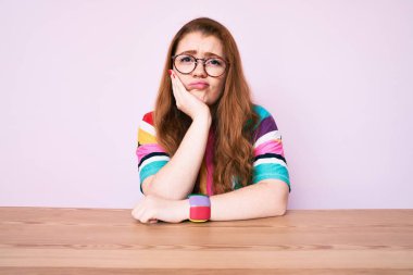 Masada oturan genç kızıl saçlı kadın kollarını kavuşturup depresyondan sıkılmış ve yorgun göründüğünü düşünüyor.. 