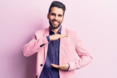 Sakallı, zarif ceketli, elleri büyük ve büyük bir işaret gösteren yakışıklı bir genç. Ölçü sembolü. Kameraya bakıp gülümsüyor. ölçüm kavramı. 