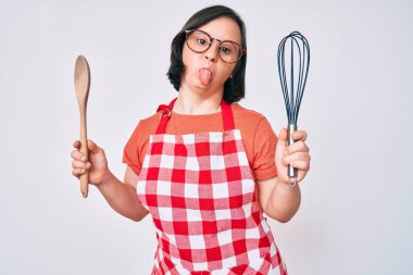 Esmer kadın, aşçılık sendromlu fırıncı çırpıcı ve kaşık kullanarak komik bir ifadeyle dilini dışarı çıkarıyor.. 