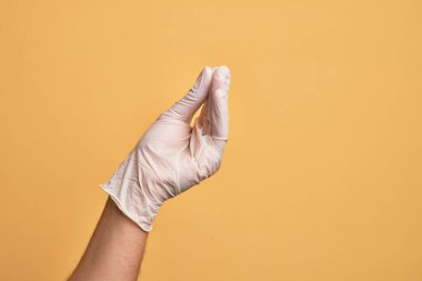 Tıbbi eldiveni olan, izole edilmiş sarı arka planda İtalyan jestleri yapan, iletişim hareketi yapan beyaz bir gencin eli.