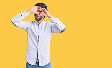 İş gömleği ve gözlük takan yakışıklı, kalp şeklinde el ve parmaklarıyla gülümseyen, tabeladan bakan yakışıklı İspanyol. 