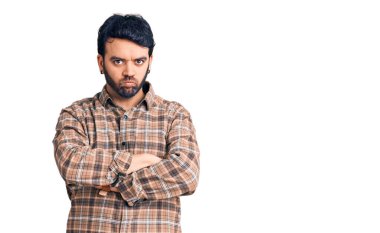 Gündelik kıyafetler giyen, kuşkucu ve gergin genç İspanyol bir adam. Yüzünde çapraz kollarla onaylamayan bir ifade var. negatif kişi. 