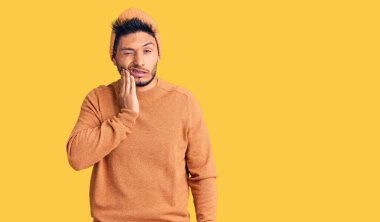 Kış süveteri giyen yakışıklı Latin Amerikalı genç adam ve diş ağrısı ya da diş hastalığından dolayı ağızlarına acı dolu bir ifadeyle dokunan yün şapkalı adam. dişçi 