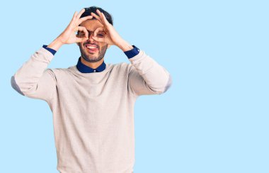 Zarif kıyafetler ve gözlük takan yakışıklı İspanyol genç adam dürbün gibi jest yapıyor. Dürbün gibi dilini dışarı çıkarıyor, gözler parmaklarından bakıyor. çılgın ifade. 