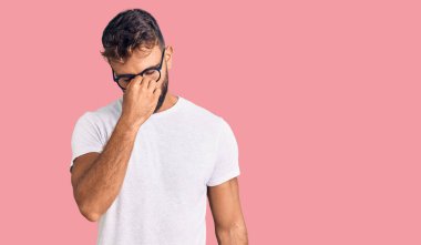 Gündelik kıyafetler ve gözlük takan genç İspanyol adam yorgun burnu ve gözleri ovuşturup yorgunluk ve baş ağrısı hissediyor. Stres ve hüsran kavramı. 