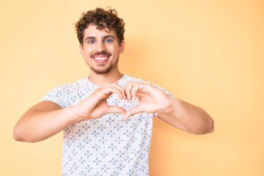 Kıvırcık saçlı, günlük kıyafetler giyen, aşık bir şekilde gülümseyen, kalp sembolü ve elleri olan genç, beyaz bir adam. romantik kavram. 