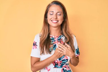 Orta yaşlı İspanyol kadın sıradan bir çiçek elbisesi giyiyor göğsünde elleri kapalı, yüzünde minnet dolu bir jest ile gülümsüyor. sağlık kavramı. 