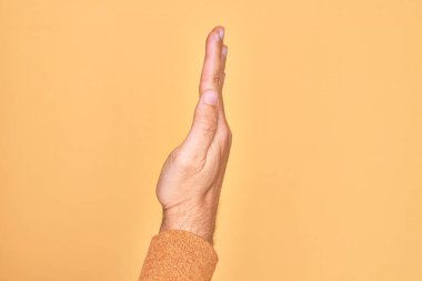 Kafkasyalı bir gencin elleri sarı arka planda parmaklarını gösteriyor. Uzanmış el hareketlerini gösteriyor, itiyor ve duruyor.