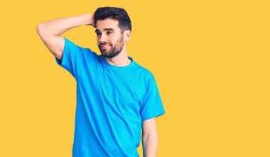 Sakallı, sıradan bir tişört giyen, kendine güvenen, el hareketleriyle saçlara dokunan çekici ve modaya uygun poz veren yakışıklı bir genç. 