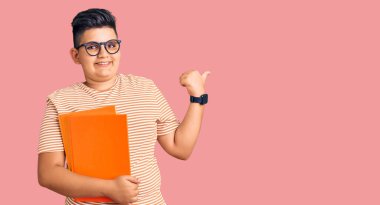 Küçük çocuk elinde gözlüklerle arka tarafı işaret ediyor. Baş parmakları havada, kendinden emin gülümsüyor. 