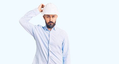 Mimar şapkası takan genç yakışıklı adam soru sorup şaşırıyor. Şüpheyle kararsız, kafa kafaya düşünerek. Düşünceli kavram. 