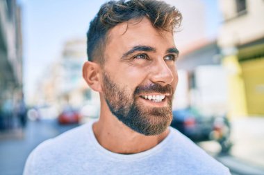 Genç İspanyol adam gülümseyerek şehirde mutlu bir şekilde yürüyor.