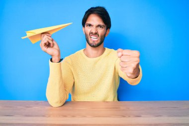 Elinde kağıt uçak tutan yakışıklı İspanyol adam öfkeyle bağırıyor, öfkeyle bağırıyor ve el kaldırıyor. 