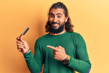 Genç Arap adam berber jiletini tutuyor gülümsüyor mutlu eli ve parmağı ile işaret ediyor. 