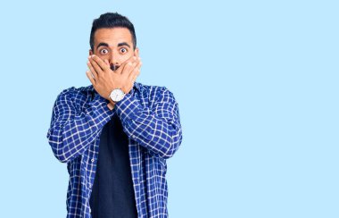 Gündelik kıyafetler giyen genç İspanyol adam yanlışlıkla elleri ile ağzını kapatırken şok oldu. gizli kavram. 