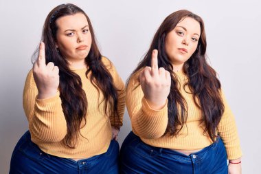Young plus size twins wearing casual clothes showing middle finger, impolite and rude fuck off expression 