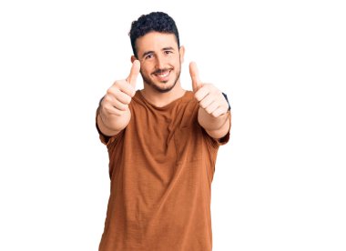 Latin asıllı genç adam gündelik giysiler giyip olumlu jestler yapıyor. Elleriyle gülümsüyor ve başarı için seviniyor. kazanan jest. 