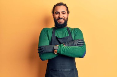 Berber önlüğü takan genç Arap adam kameraya bakarken kollarını kavuşturup gülümsüyor. pozitif kişi. 