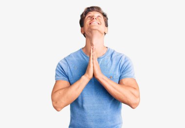 Gündelik giysiler giymiş genç yakışıklı bir adam elleri bağlı yalvarıyor ve dua ediyor. Yüzünde umut ifadesi var. Duygusal ve endişeli. Yalvarıyor. 