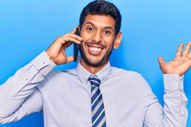Genç latin adam akıllı telefonda konuşuyor başarıyı kutlamak için gülümsüyor ve kazanan yüz ifadesini kaldırıyor. 
