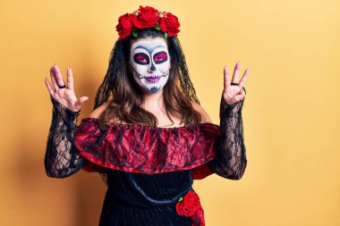 Sarı üzerine ölü kostümü giymiş genç bir kadın sekiz numaralı parmaklarıyla işaret ederken kendinden emin ve mutlu bir şekilde gülümsüyor.. 