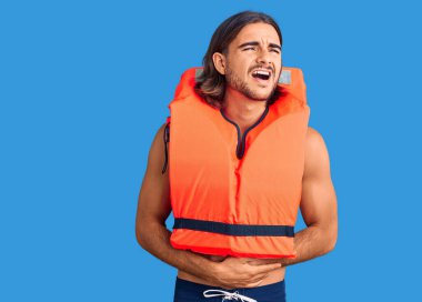 Deniz cankurtaran yeleği giyen genç yakışıklı bir adam mide bulantısı, acı verici bir hastalık yüzünden midesi üzerinde. Ağrı kavramı. 