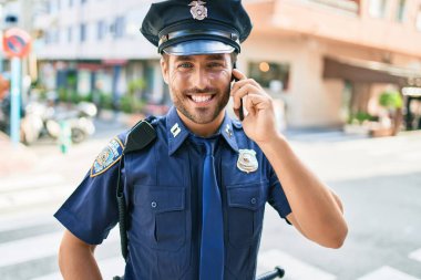 Genç, yakışıklı İspanyol polis memuru polis üniforması giyip mutlu gülümsüyor. Yüzünde tebessümle dikilip şehrin caddesinde akıllı telefondan konuşuyor..
