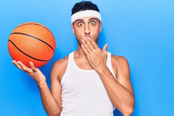 Pemuda Hispanik Memegang Bola Basket Menutupi Mulut Dengan Tangan Terkejut — Stok Foto