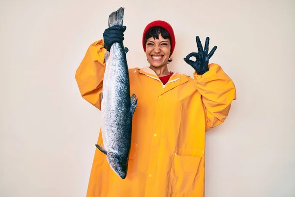 Hermosa Morena Pescadora Vistiendo Impermeable Sosteniendo Salmón Fresco Haciendo Signo —  Fotos de Stock