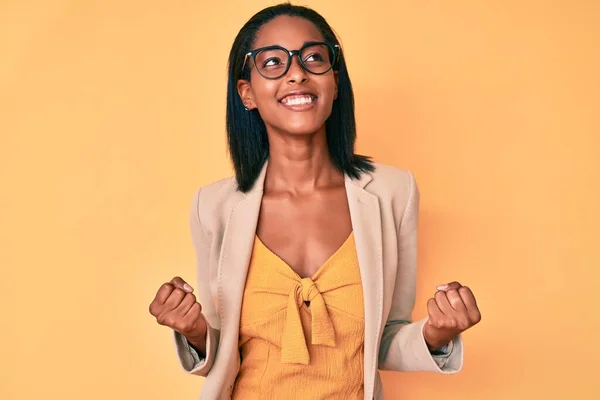 若いアフリカ系アメリカ人女性はビジネス服を着て非常に満足し 腕を上げて勝者のジェスチャーを行う興奮し 笑顔と成功のために叫んでいます お祝いのコンセプト — ストック写真