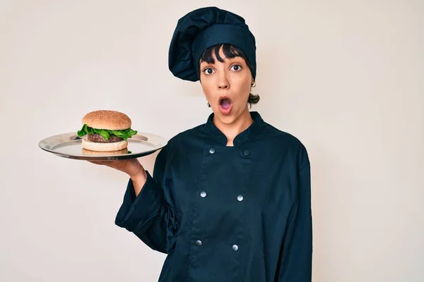 Piękna Brunetka Kobieta Szef Kuchni Trzymając Burgera Przestraszony Zdumiony Otwartymi — Zdjęcie stockowe