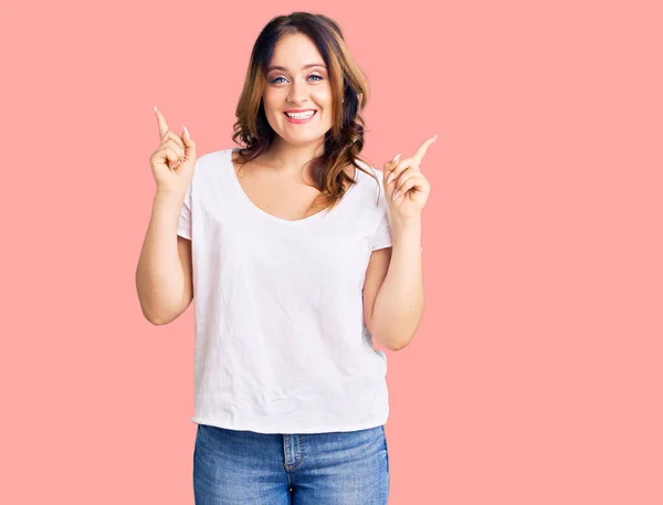 年轻美丽的高加索女人穿着休闲的白色T恤 自信地微笑着 手指指向不同的方向 复制广告空间 — 图库照片