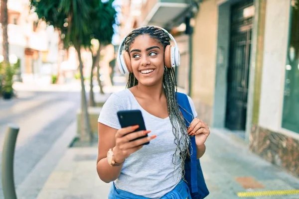 Genç Afrikalı Amerikalı öğrenci kampüste akıllı telefon kullanarak mutlu bir şekilde gülümsüyor.