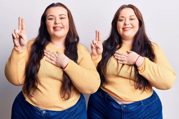 Young plus size twins wearing casual clothes smiling swearing with hand on chest and fingers up, making a loyalty promise oath