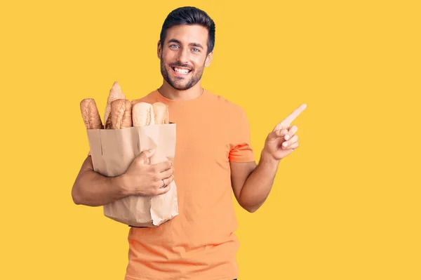 Young Hispanic Man Holding Paper Bag Bread Smiling Happy Pointing — Stock Photo, Image