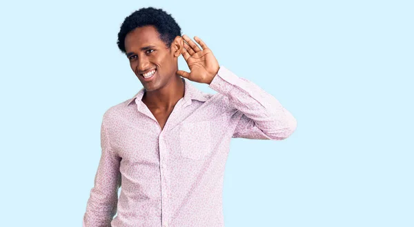 身穿休闲粉色衬衫的非洲帅哥 两手空空地听着谣言或流言蜚语 面带微笑 聋的概念 — 图库照片