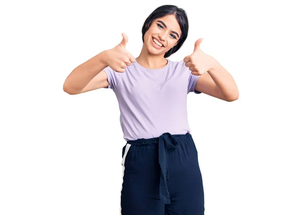 ブルネットのティーンエイジャーの女の子は 手で肯定的なジェスチャーを行うことを承認カジュアルな服を着て 親指を笑顔と成功のために幸せ 勝者のジェスチャー — ストック写真