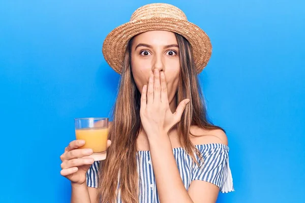夏の帽子をかぶっている若い美しい女の子は 手で口を覆い ショックを受け 間違いを恐れてオレンジジュースを飲んでいます 驚きの表情 — ストック写真