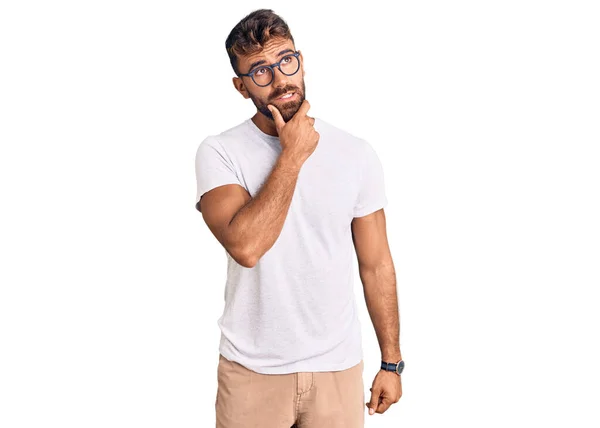 カジュアルな服と眼鏡を身に着けている若いヒスパニック系の男は 質問を心配し 顎に手で心配し 神経質 — ストック写真