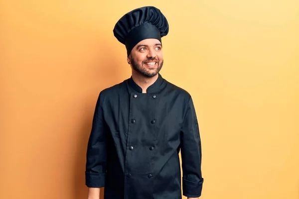 Young hispanic man wearing cooker uniform looking to side, relax profile pose with natural face and confident smile.