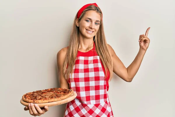 Jovem Loira Vestindo Avental Profissional Padeiro Segurando Pizza Italiana Sorrindo — Fotografia de Stock