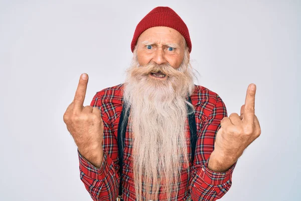 Old senior man with grey hair and long beard wearing hipster look with wool cap showing middle finger doing fuck you bad expression, provocation and rude attitude. screaming excited 