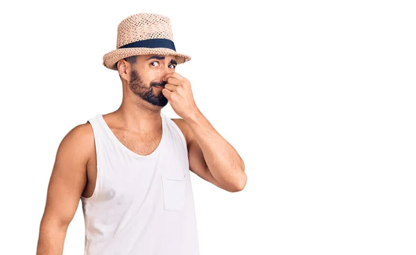 若いヒスパニック系の男は 鼻の上に指で息を保持し 臭いと嫌な 耐え難い匂いの何かを嗅ぐカジュアルな夏の帽子を身に着けている 臭いが悪い — ストック写真