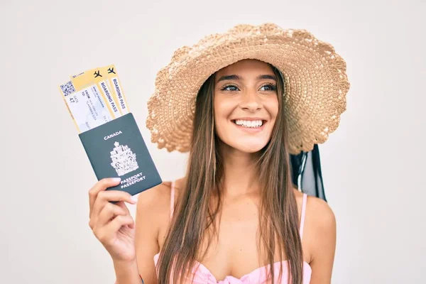 Young hispanic woman on vacation holding canadian passport and boarding pass at street of city