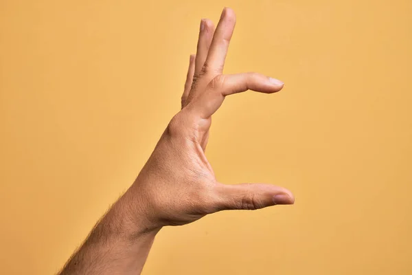 孤立した黄色の背景のピッキングの上に指を示す白人の若者の手と目に見えないものを取ります 空間を示す指でオブジェクトを保持 — ストック写真