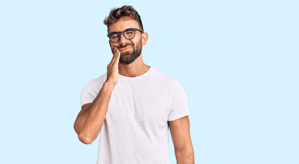 歯痛や歯の病気のために痛みを伴う表現で手で手に触れるカジュアルな服や眼鏡を身に着けている若いヒスパニック系の男性 歯科医 — ストック写真