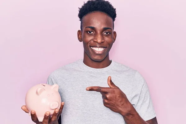 Jonge Afro Amerikaanse Man Houdt Spaarvarken Bank Glimlachen Gelukkig Wijzend — Stockfoto